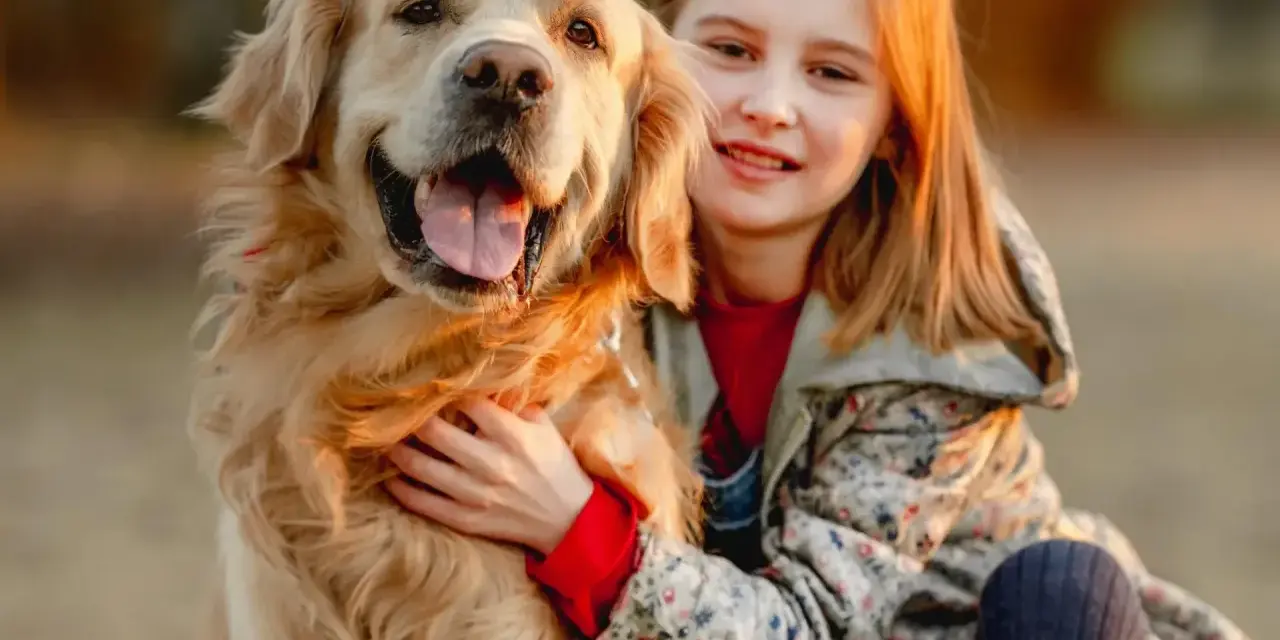Uśmiechnięta dziewczynka tuli swojego złotego retrievera. Zastanawiasz się, ile kosztuje golden retriever?