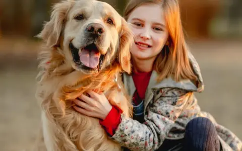 Uśmiechnięta dziewczynka tuli swojego złotego retrievera. Zastanawiasz się, ile kosztuje golden retriever?