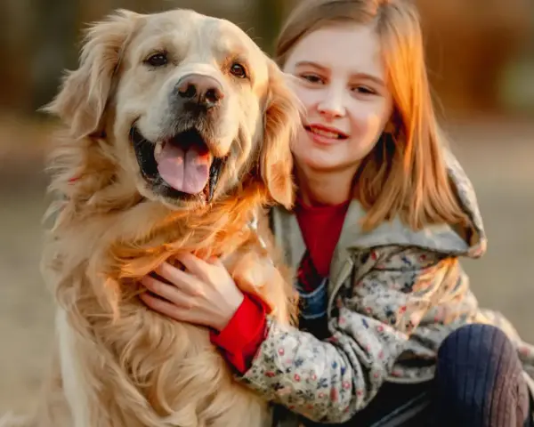 Uśmiechnięta dziewczynka tuli swojego złotego retrievera. Zastanawiasz się, ile kosztuje golden retriever?