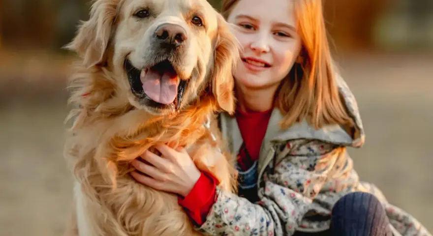Uśmiechnięta dziewczynka tuli swojego złotego retrievera. Zastanawiasz się, ile kosztuje golden retriever?